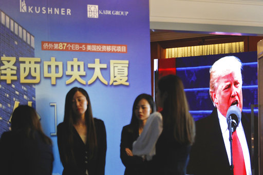 A projector screen shows a footage of U.S. President Donald Trump as workers wait for investors at a reception desk during an event promoting EB-5 investment in a Kushner Companies development at a hotel in Shanghai