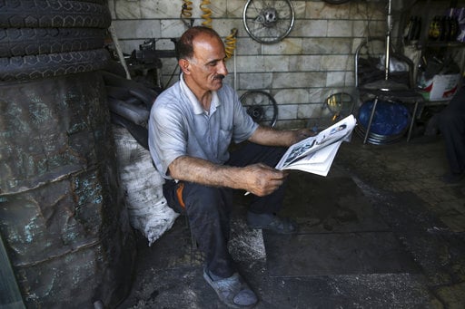 A motorcycle repairman reads a newspaper at his shop near Iran's parliament building in Tehran