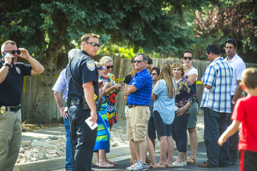 Community members look on as police officers investigate the scene of a shooting in Sandy