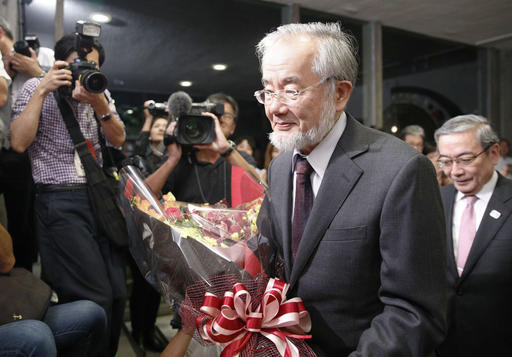 Nobel Prize winner Yoshinori Ohsumi smiles with a bouquet of flowers as he arrives at a press conference at the Tokyo Institute of Technology in Tokyo Monday