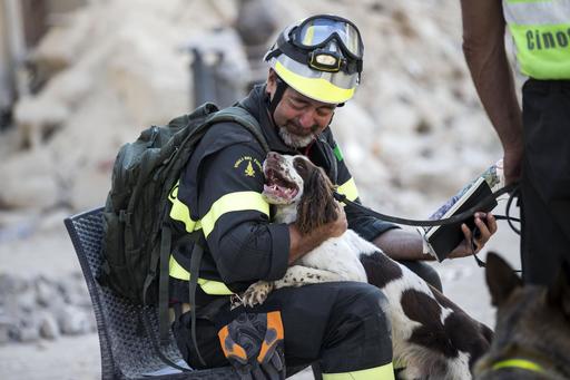 A firefighter cuddles his dog as rescuers continue searching through the rubble in Amatrice