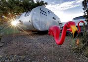 The sun sets behind a 1950 Hughes Spartan travel trailer complete with pink flamingo and vintage El Dorado Cadillac parked by its side at the Shady Dell Trailer Court