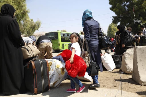 A girl clutches a teddy bear as she waits to board a bus leaving the Moadamiyeh suburb of Damascus