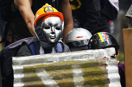 Masked demonstrators take cover during clashes with security forces at an opposition May Day march in Caracas