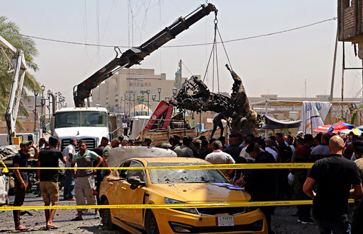 Iraqi security forces remove destroyed vehicles at the site of a deadly bomb attack