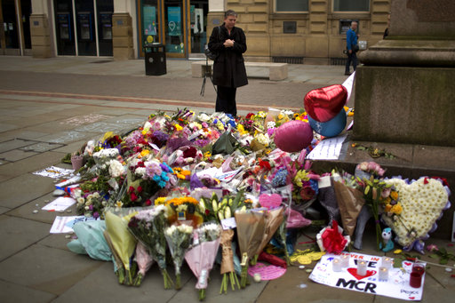 A woman stands next to flowers offered for the victims of a suicide attack at a concert by Ariana Grande that killed more than 20 people Monday night in central Manchester