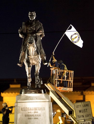 A worker in protective gear takes down an Army National Guard flag from the statue of Confederate General P.G.T. Beauregard during the statue's removal from the entrance to City Park in New Orleans