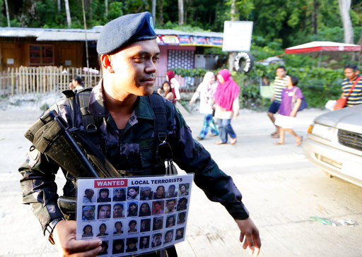 A police officer holds a poster of wanted Filipino Muslim militants known as "Maute " group at a checkpoint set up at the entrance to Iligan city Saturday