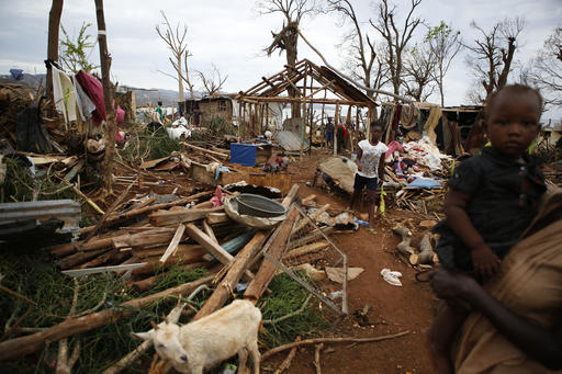 Residents stand amidst the rubble of destroyed homes as they watch a U.S. military helicopter land to deliver USAID relief supplies