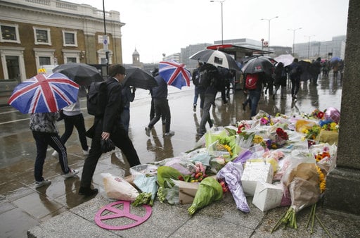 Pedestrians walk in the rain by a flower memorial in the London Bridge area of London on Tuesday