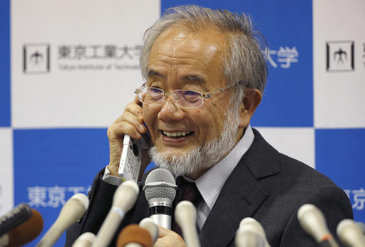 Nobel Prize winner Yoshinori Ohsumi smiles as he speaks with Japanese Prime Minister Shinzo Abe on a mobile phone during a press conference at the Tokyo Institute of Technology in Tokyo Monday