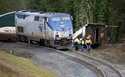 Workers walk over tracks near a curve at the back of where an Amtrak train derailed above Interstate 5