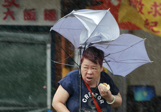 A woman eats and struggles with her umbrella against powerful gusts of wind generated by typhoon Megi across the the island in Taipei