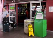Unidentified travelers exit the airport past a green metal container designed for "Disposal for Prescription and Recreational Drugs