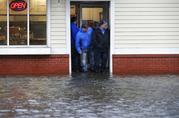 People stand at the entrance to a pizza shop as water floods a street