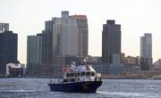 A police patrol boat is positioned near a sunken helicopter in the East River