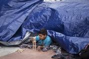 A migrant child from El Salvador plays under a tarpaulin at the El Chaparral port of Entry