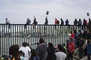 Central American migrants traveling with a caravan gather at the border wall