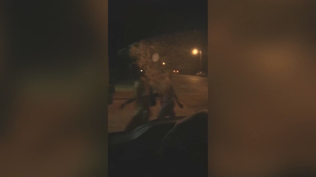A screenshot from the videos shows an LMPD officer throw a drink at two people walking on the sidewalk late at night (WHAS)