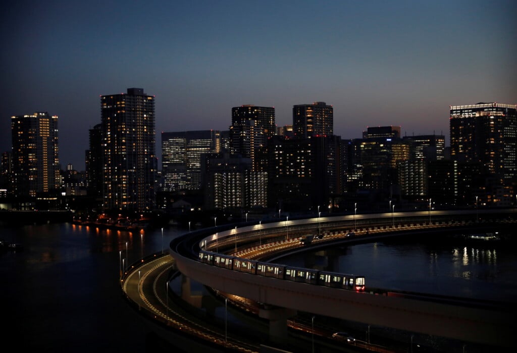 A Yurikamome Line Train Runs With City Skyline In Background, In Tokyo