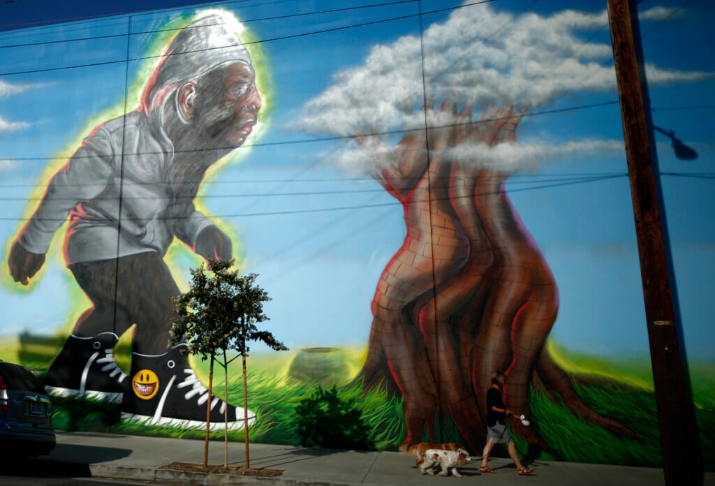 A Woman Walks Her Dogs Past English's Mural "urban Bigfoot" In Los Angeles