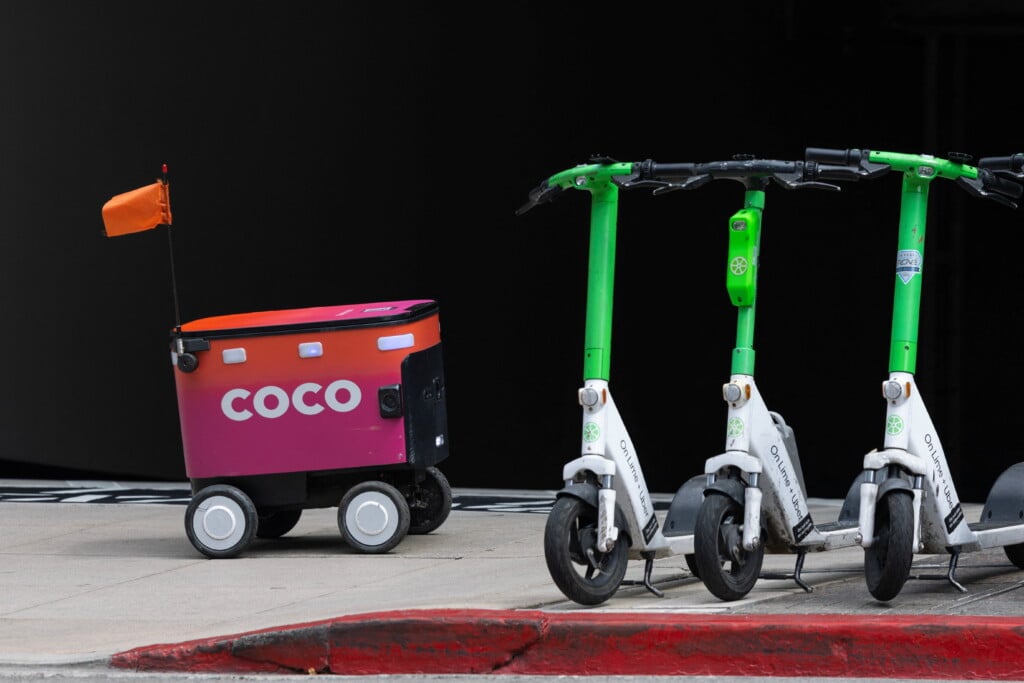 An Autonomous Food Delivery Robot Passes A Pod Of Electric Scooters In Downtown Los Angeles