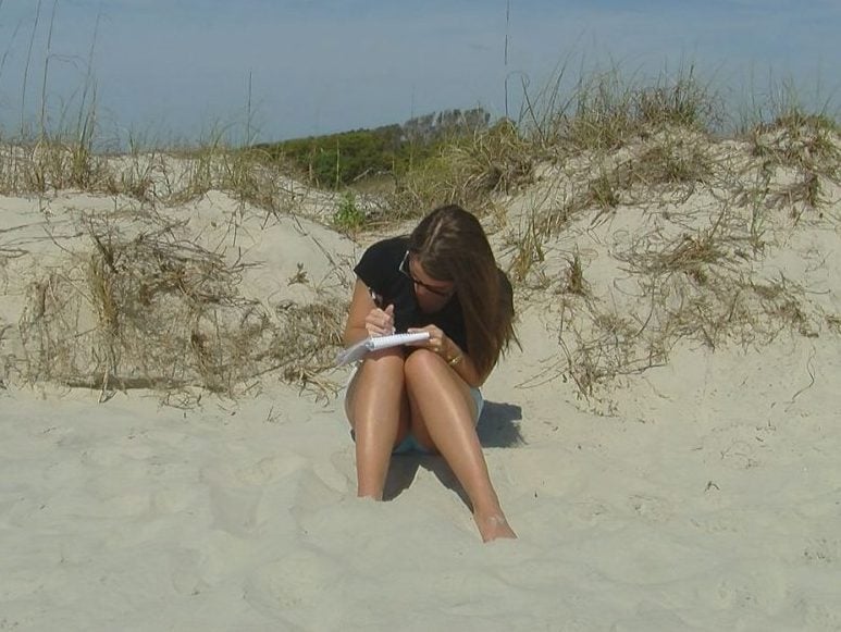 girls sitting on beach writing in book