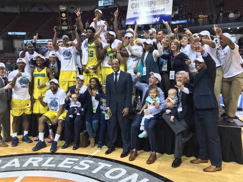 The UNCW basketball team poses with the CAA Basketball Championship trophy.
